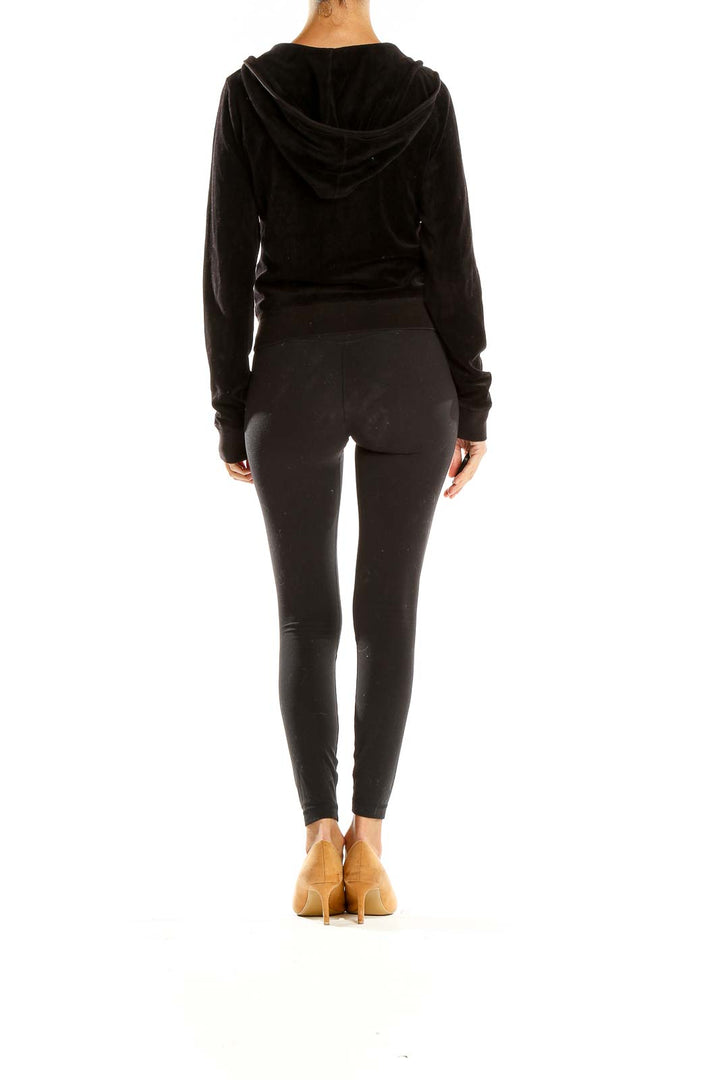 Side view of model wearing Juicy Couture black velour zip-up hoodie jacket with black leggings