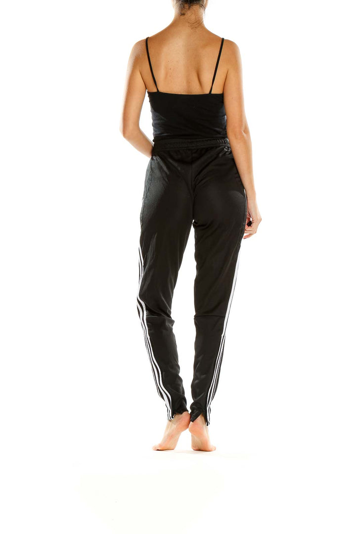 Back view of black Adidas track pants with white stripes