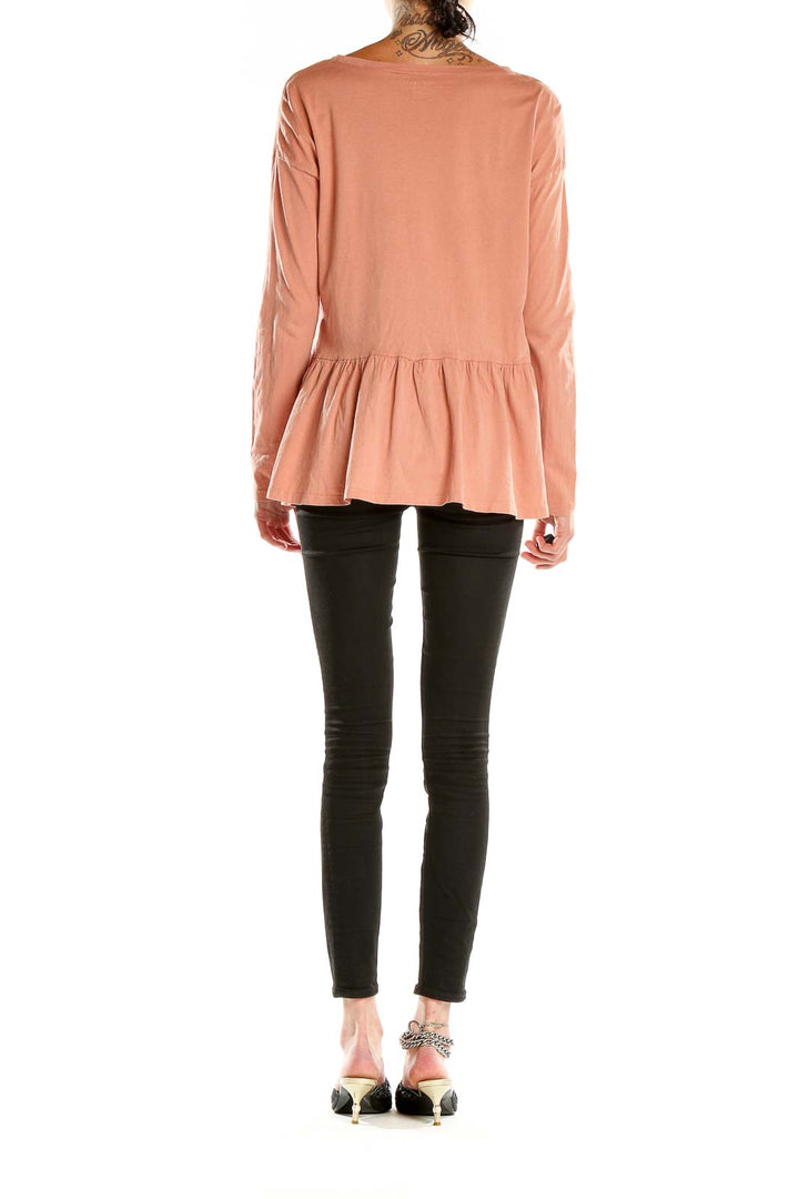 Side view of peach long-sleeve peplum top by For the Republic with black pants