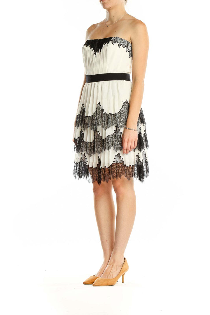 Front view of BCBG MaxAzria white lace strapless cocktail dress with black trim and tiered skirt
