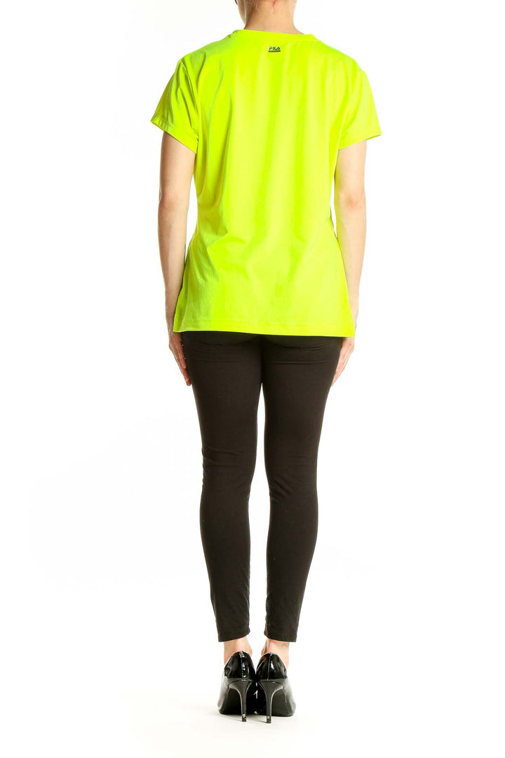 Side view of woman wearing neon yellow Fila V-neck athletic top with black pants