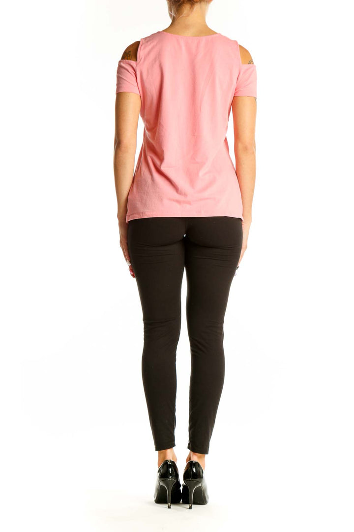 Side view of woman wearing pink MICHAEL Michael Kors cold shoulder top with black pants