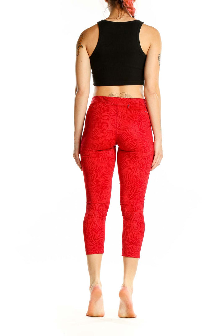 Back view of red textured Nike capri leggings on model with black crop top