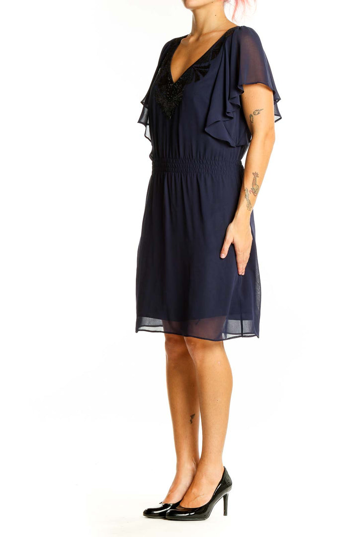 Front view of navy chiffon cocktail dress with flutter sleeves and sequin embellished V-neckline