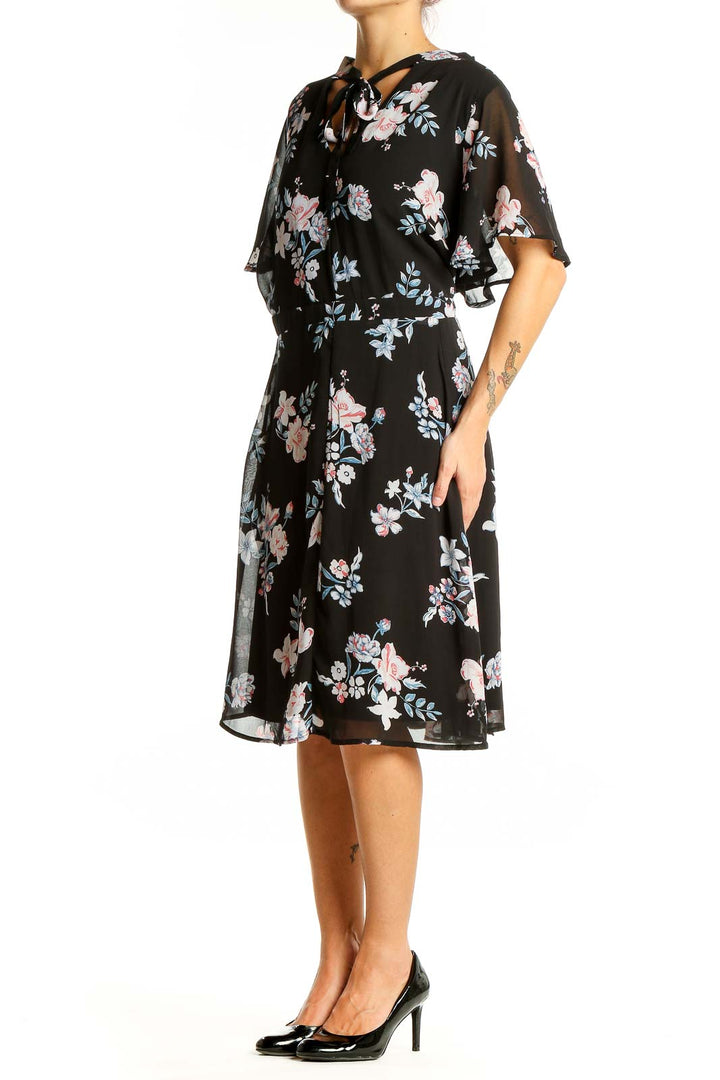 Front view of Torrid black floral midi dress with flutter sleeves and tie-neck detail