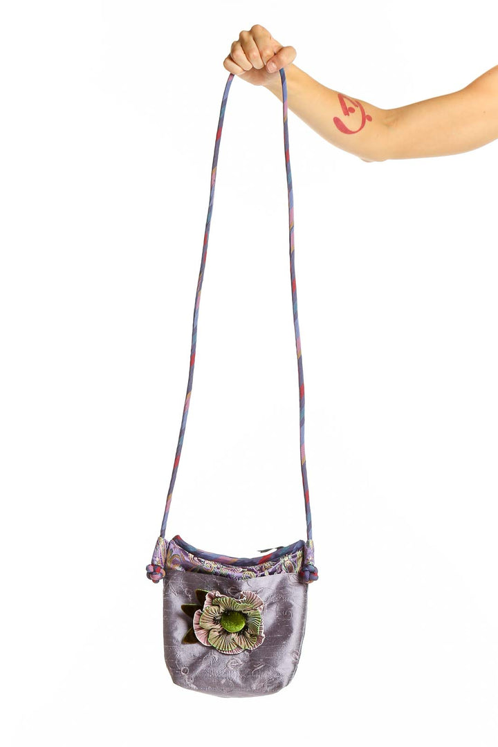 Purple crossbody bag with floral embellishment held by model's arm