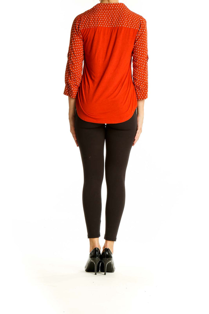 Back view of orange polka dot blouse on model with black pants