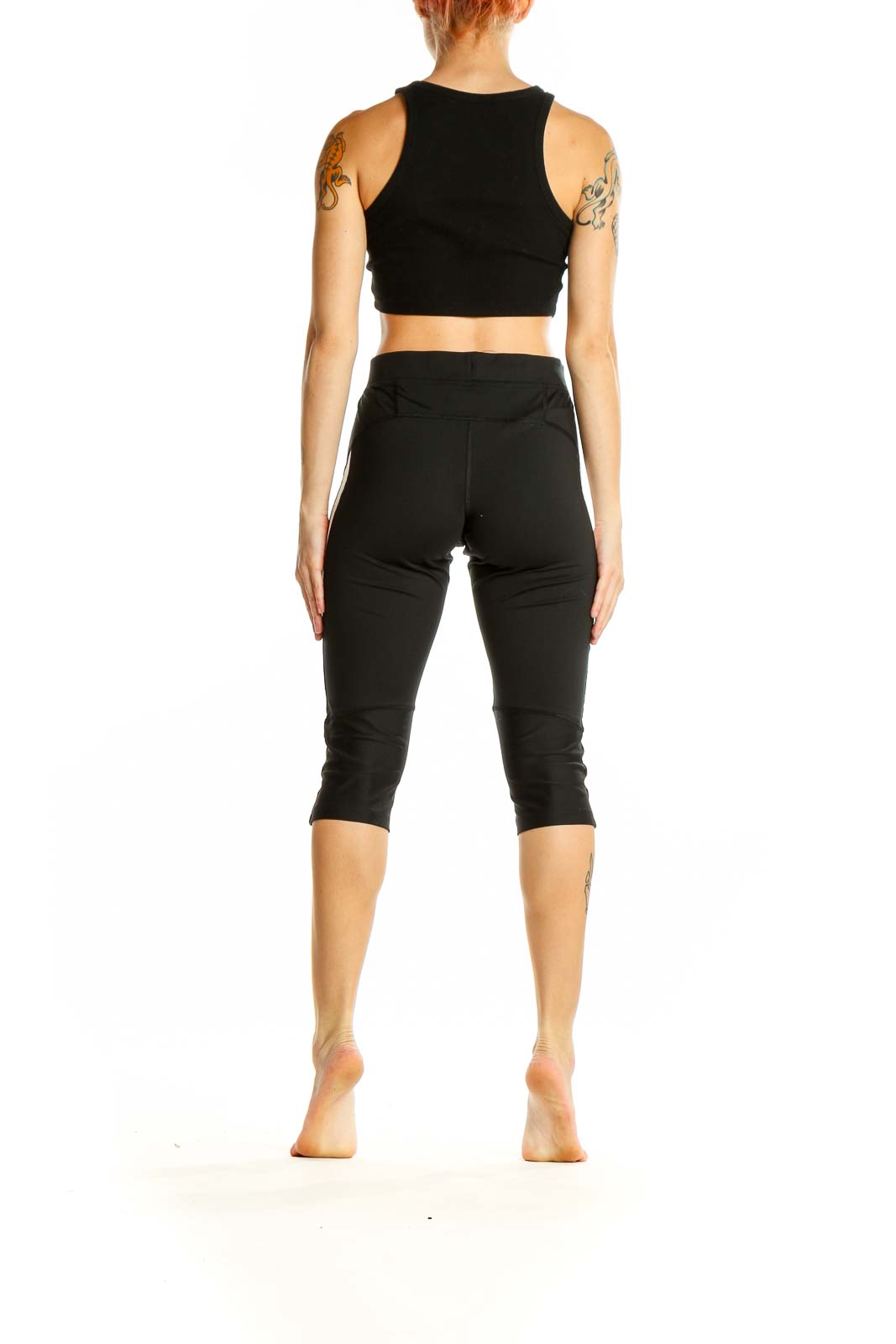 Side view of woman wearing black Nike capri leggings with white stripe and matching crop top