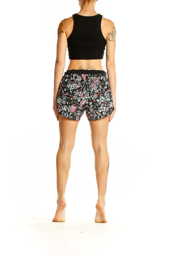 Side view of woman wearing Under Armour black floral print athletic shorts with black crop top