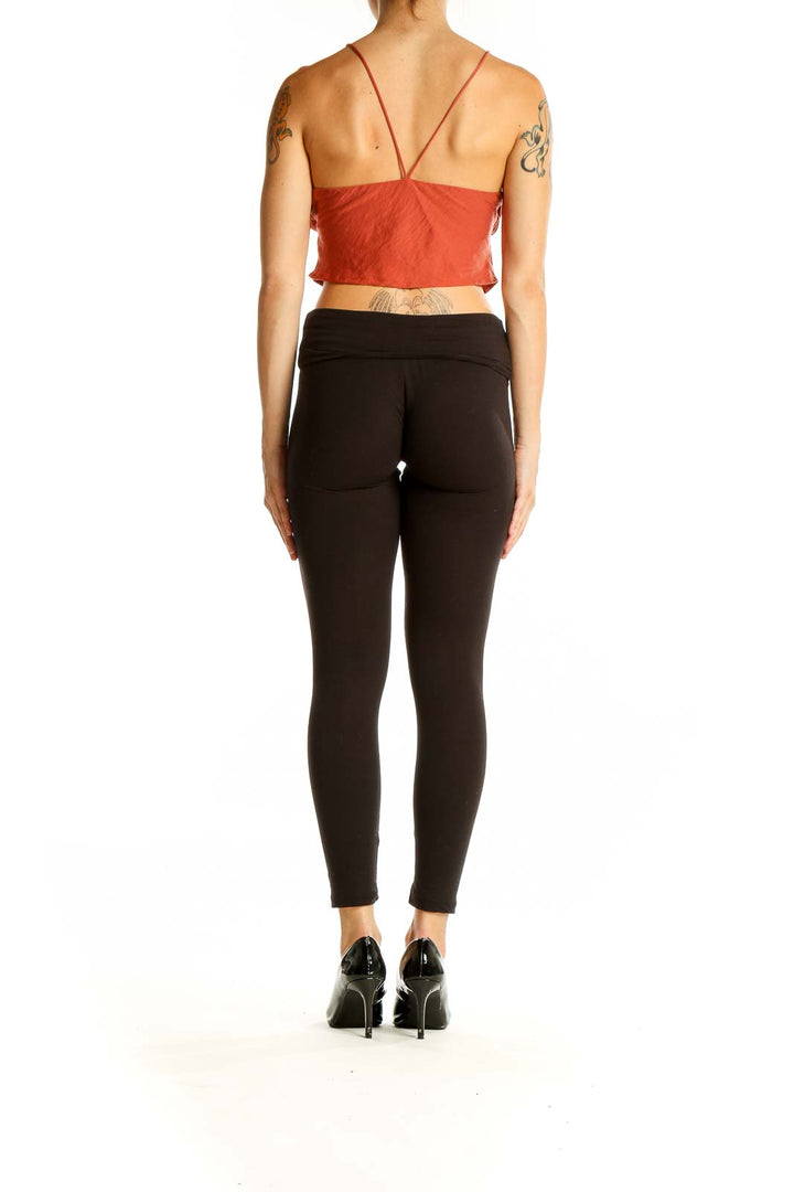 Back view of rust-colored cropped cami top on model with black pants