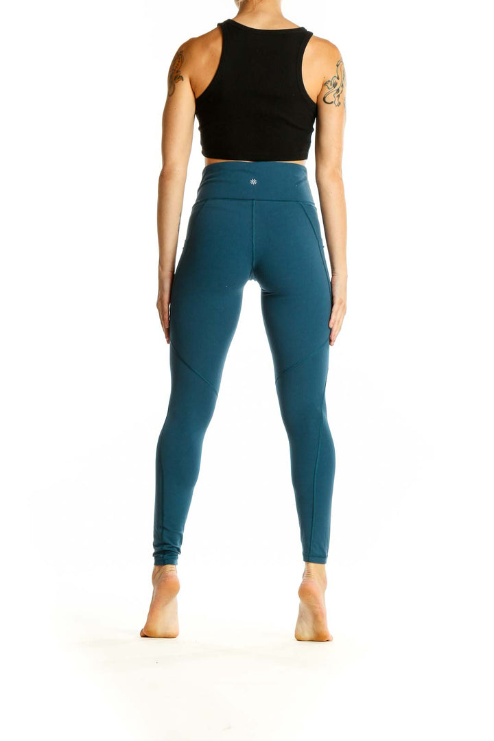 Side view of woman wearing teal Athleta high-waisted leggings and black crop top