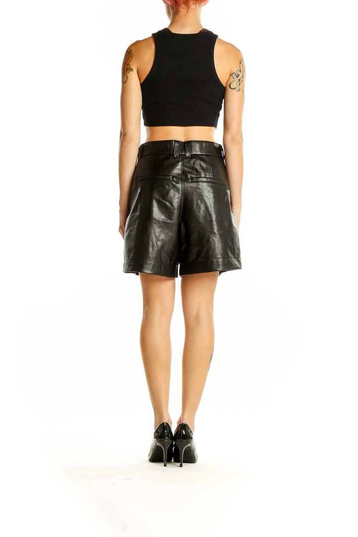 Side view of model wearing Abercrombie & Fitch black faux leather high-waisted pleated shorts with black crop top