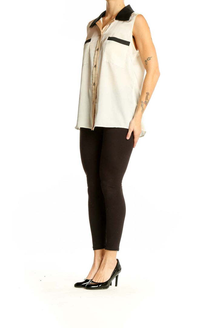 Front view of cream sleeveless blouse with black collar and pocket details