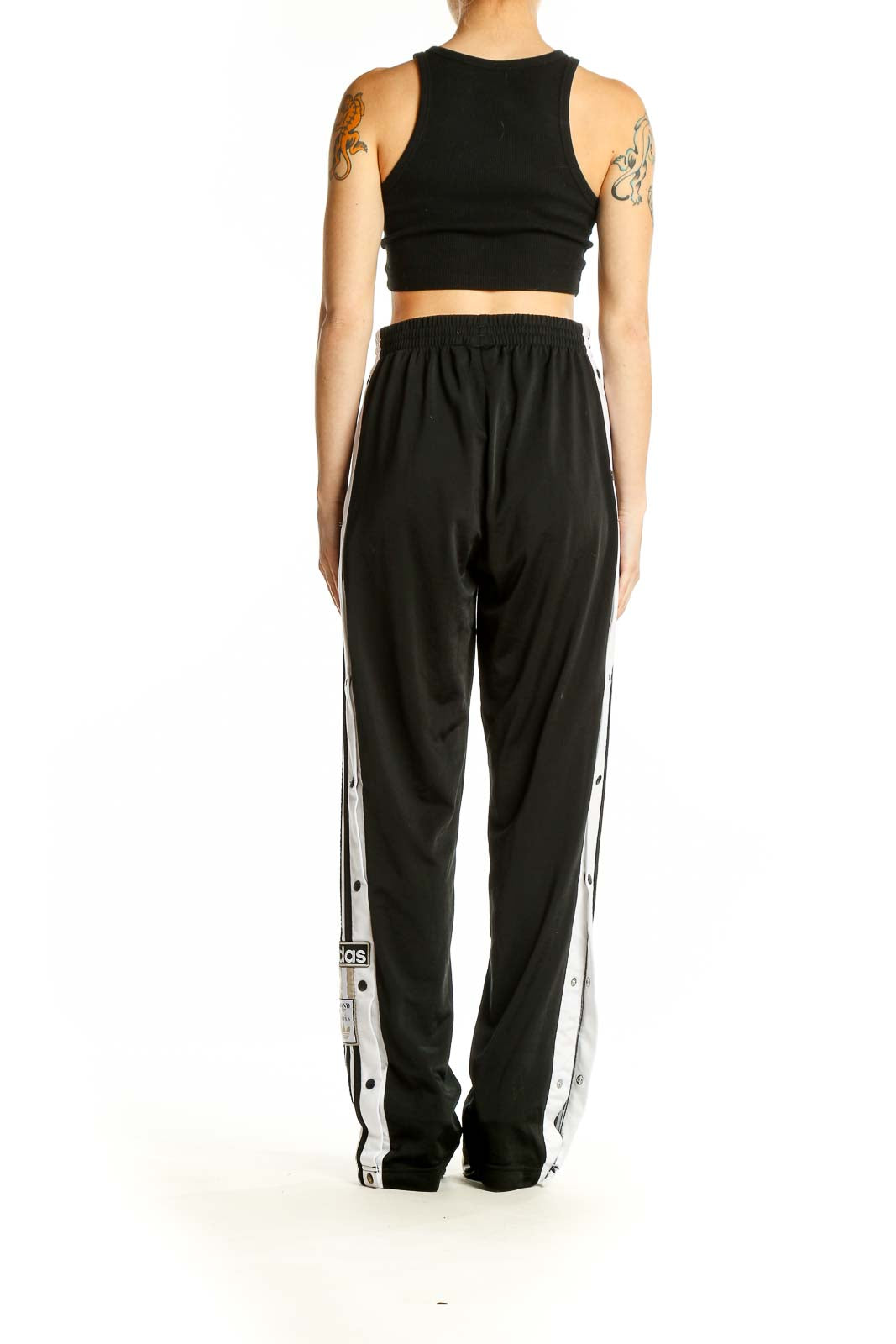 Side view of black Adidas track pants showing snap buttons and side stripe detail