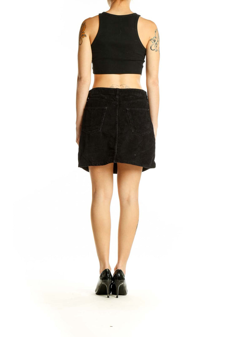 Side view of model wearing BDG black corduroy mini skirt with black top