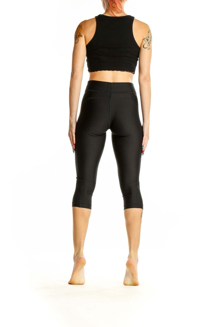 Side view of black Under Armour capri compression leggings with matching crop top