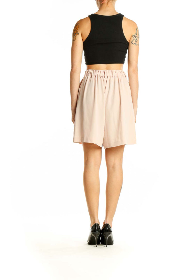 Side view of woman wearing blush Uniqlo high-waisted pleated dress shorts with black top