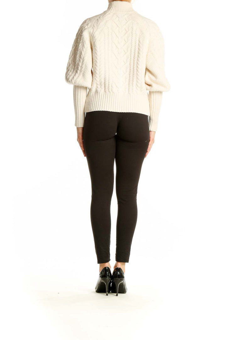 Side view of model wearing BCBG MaxAzria cream cable knit turtleneck sweater with black pants