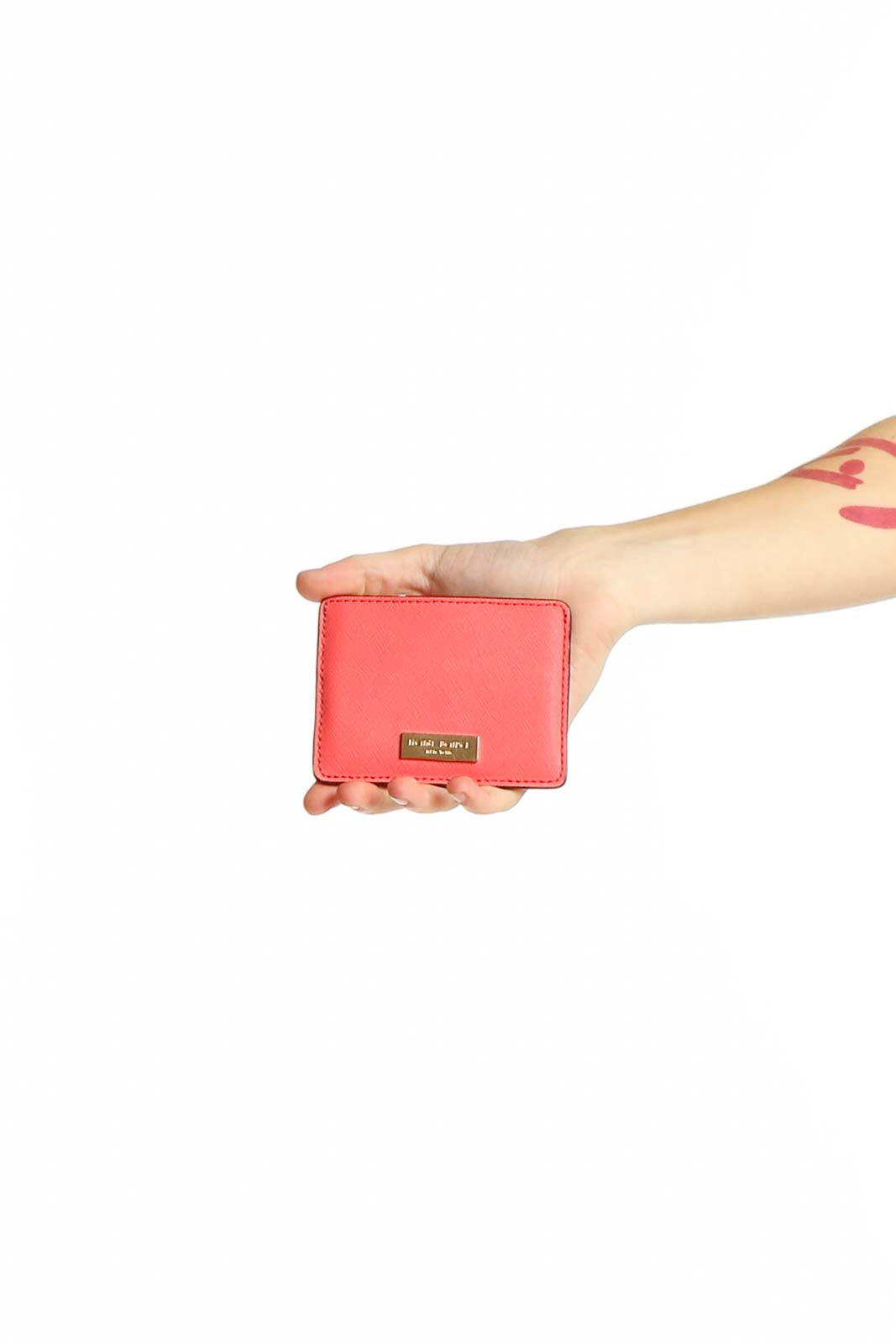 Front view of Henri Bendel coral leather clutch held in hand