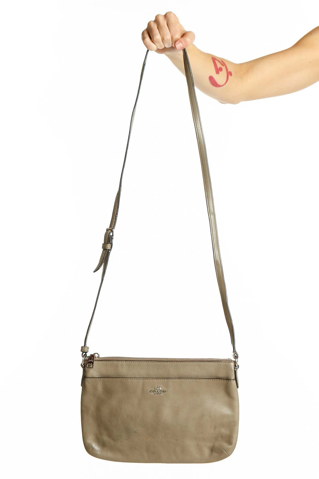 Front view of taupe leather Coach crossbody bag held by model's hand