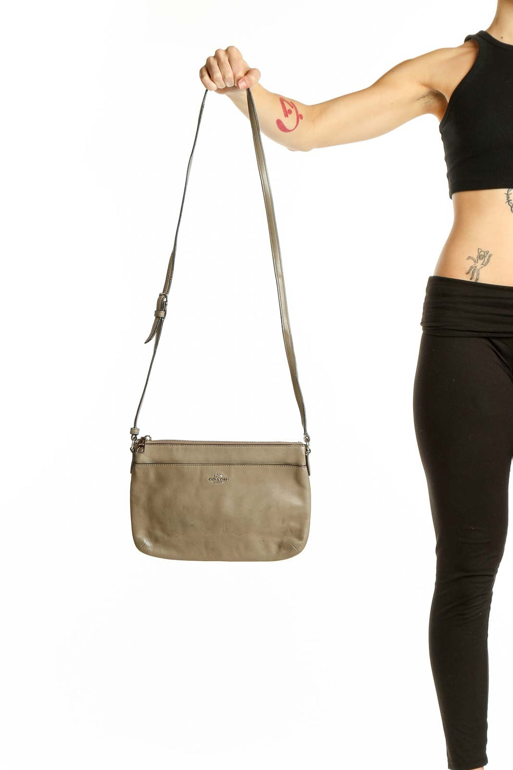 Front view of taupe leather Coach crossbody bag held by model's hand