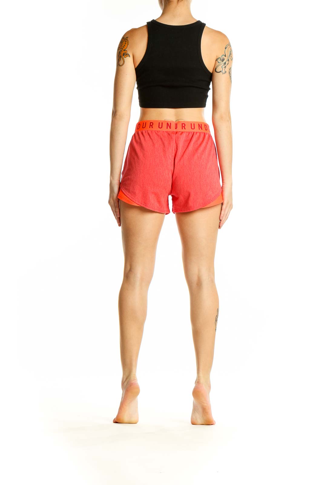 Side view of woman wearing coral Under Armour athletic shorts and black crop top