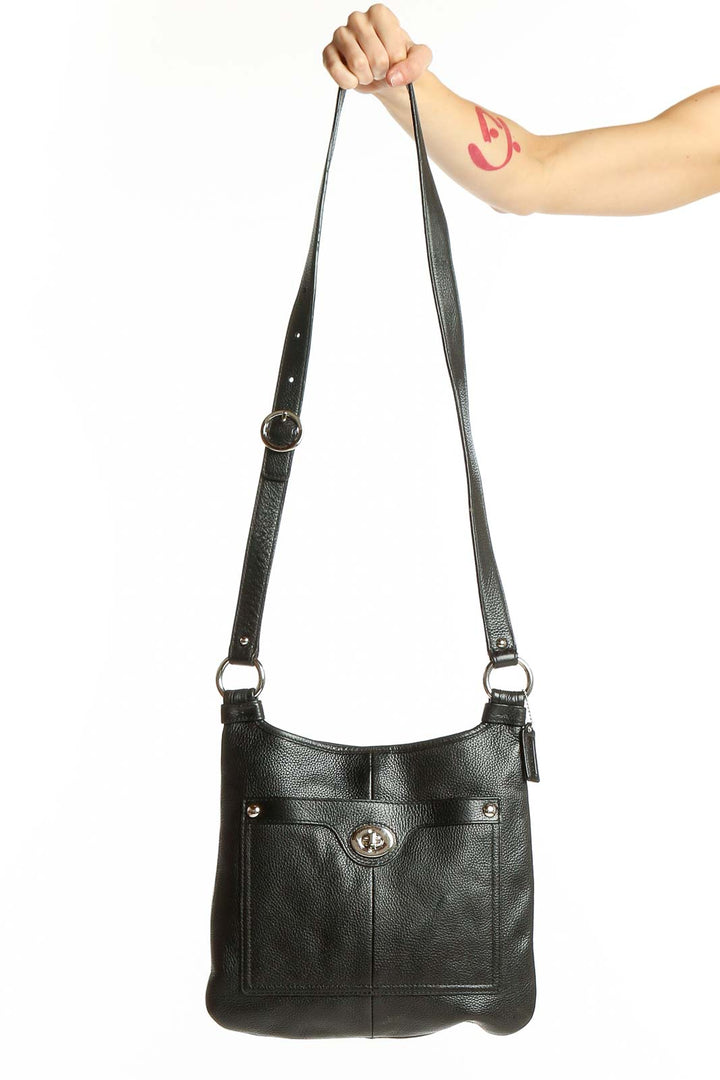 Front view of black leather Coach crossbody bag held by model's arm