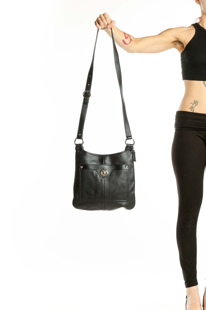 Front view of black leather Coach crossbody bag held by model's arm