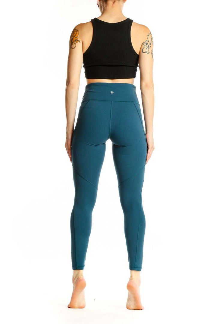 Side view of woman wearing teal Athleta high-waisted leggings and black crop top