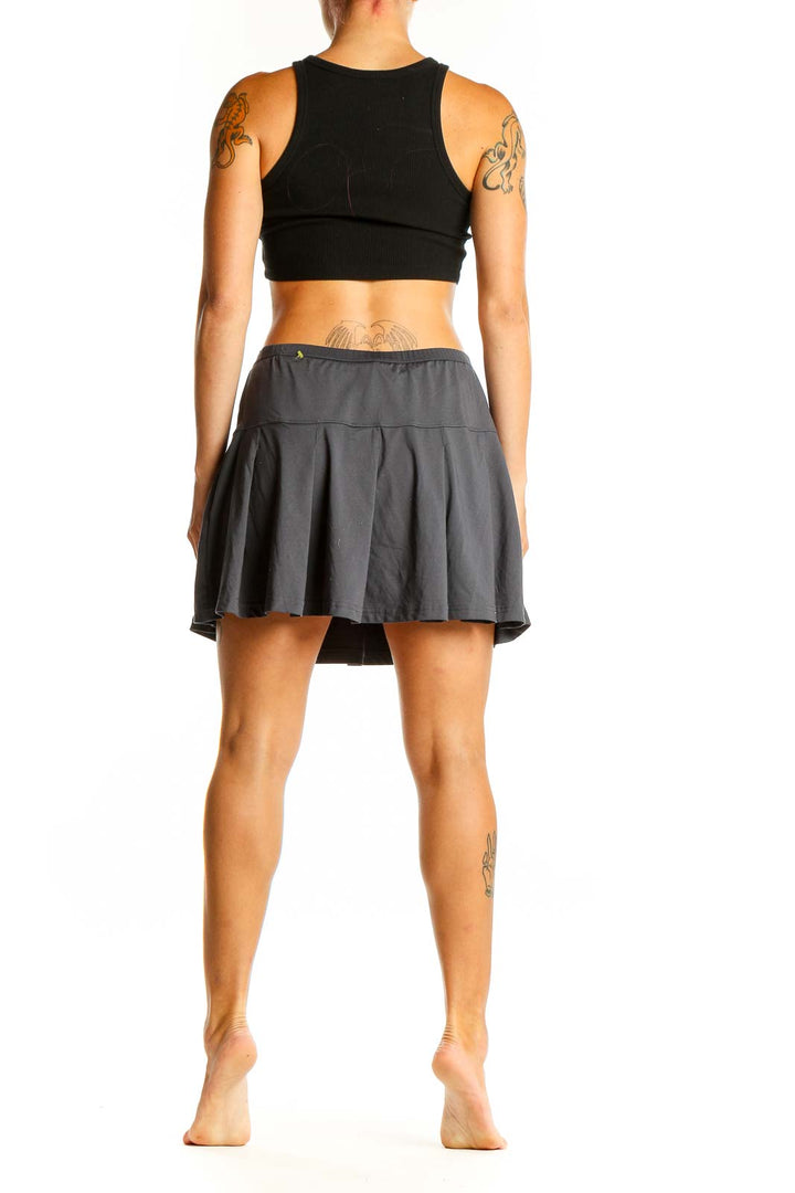 Side view of woman wearing gray pleated Bollé athletic skirt with black top