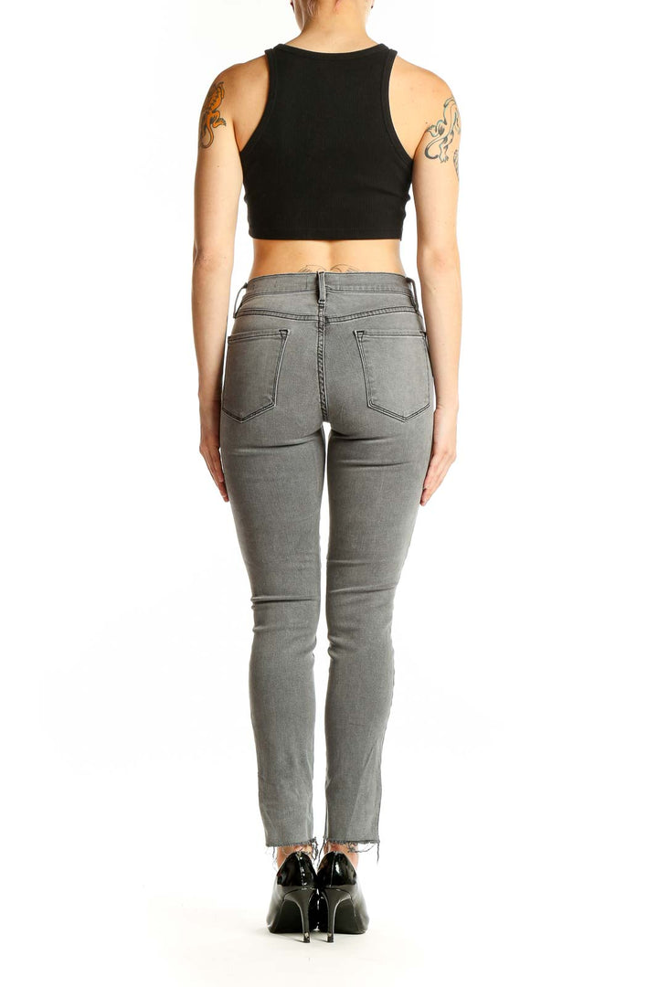 Side view of woman wearing gray FRAME Denim skinny jeans with ankle slits