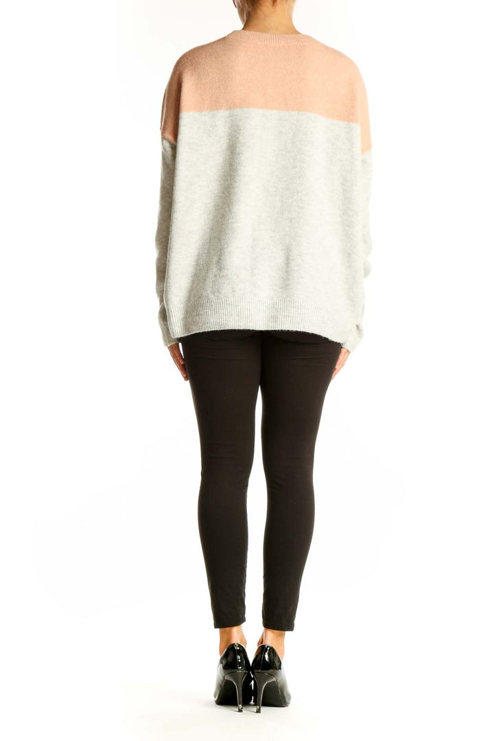 Side view of model wearing Vince Camuto peach and gray color block knit sweater with black pants