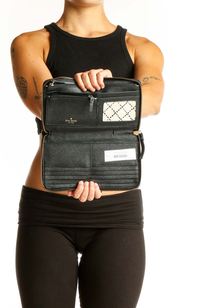 Kate Spade black leather clutch wallet held by woman in black outfit