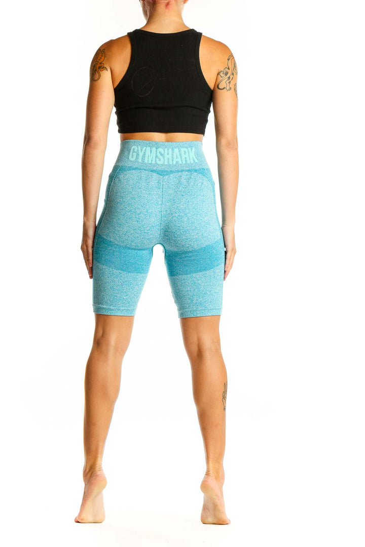 Side view of woman wearing teal Gymshark high-waisted compression biker shorts with black crop top