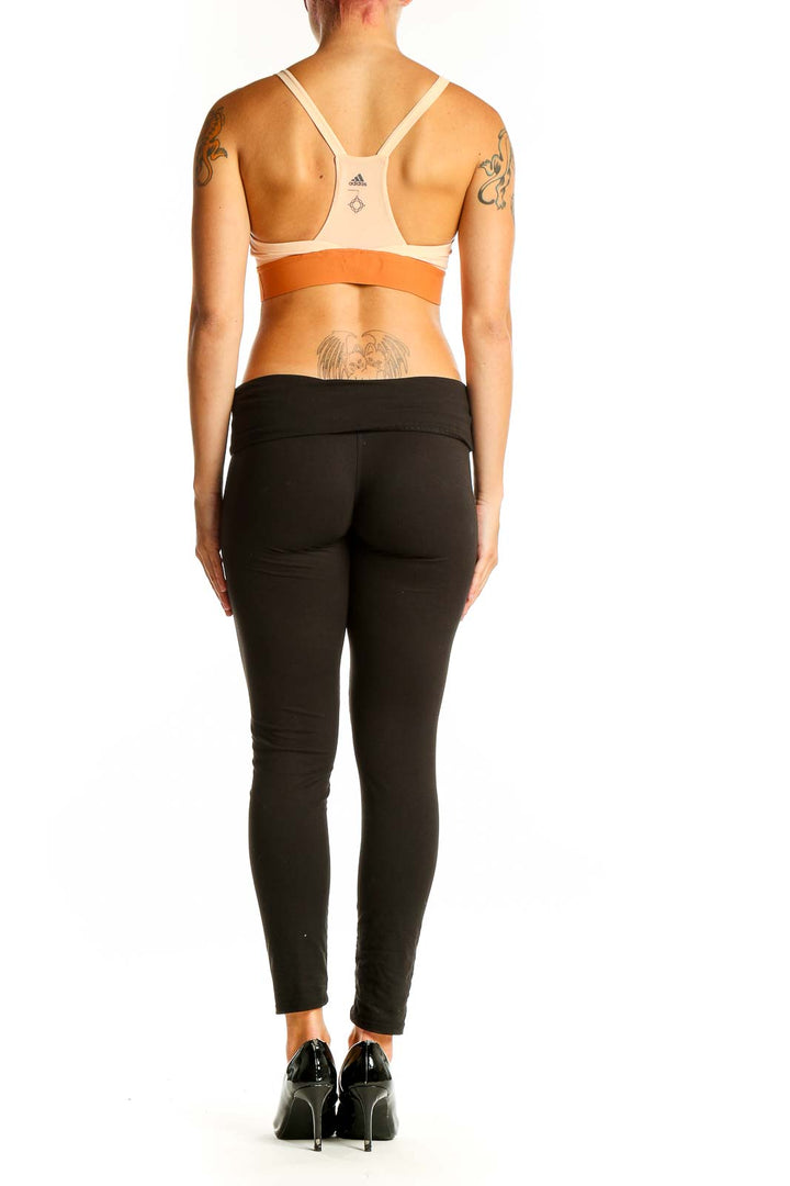 Side view of model wearing Adidas beige and orange sports bra with black leggings
