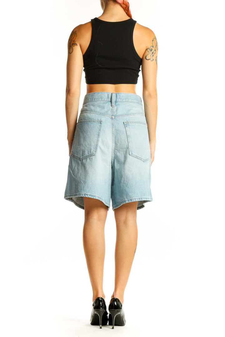 Side view of woman wearing light blue Madewell denim Bermuda shorts with black crop top