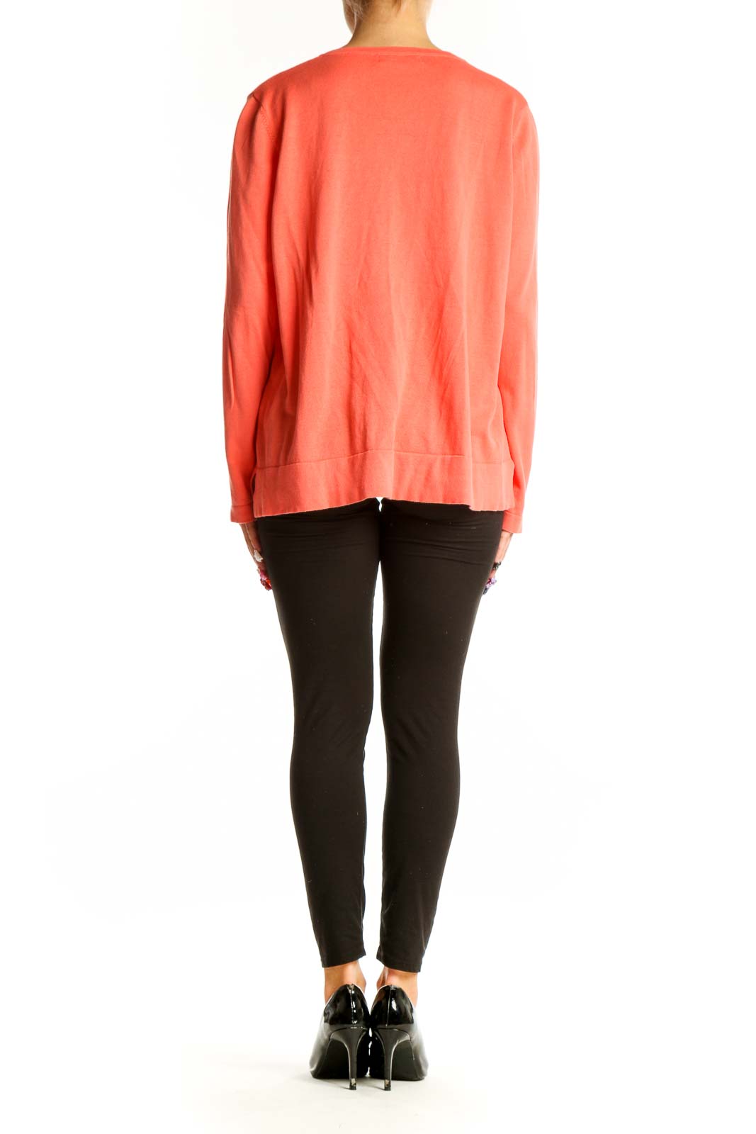 Side view of woman wearing coral button-up cardigan with black pants