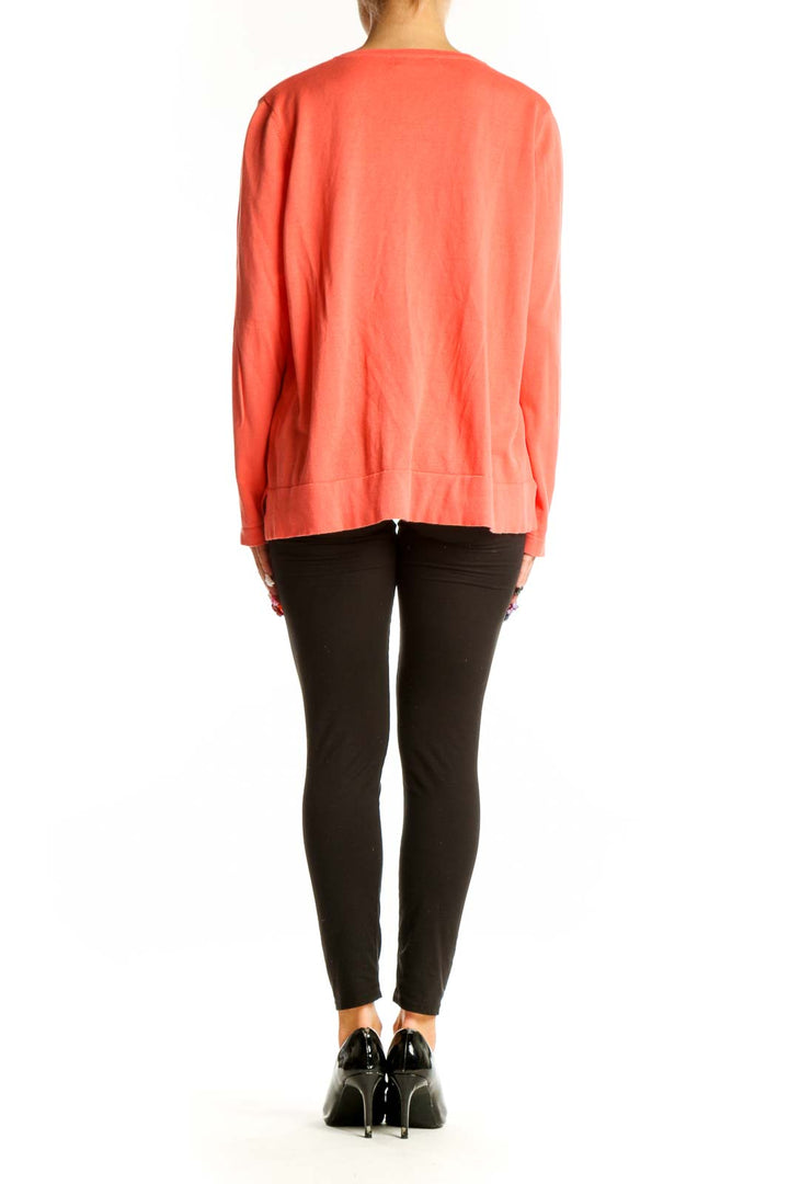 Side view of woman wearing coral button-up cardigan with black pants