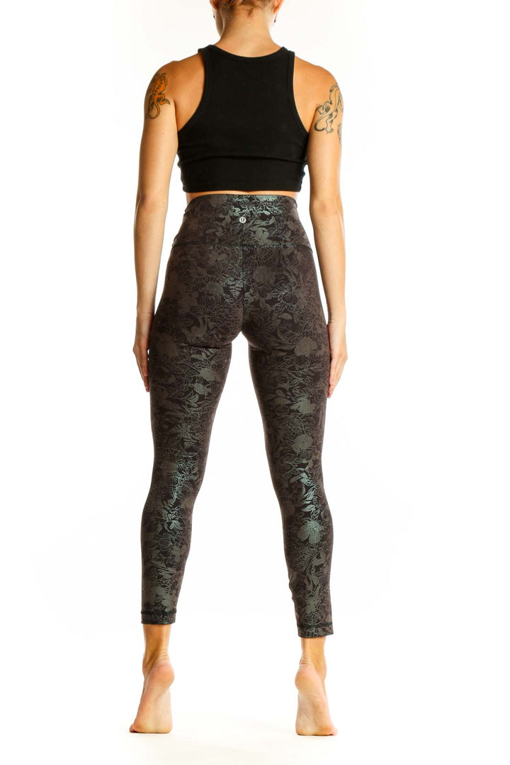 Side view of woman wearing Lululemon dark green floral print high-waisted activewear leggings with black crop top