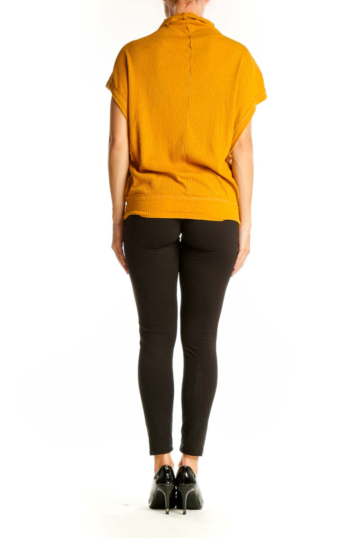 Side view of woman wearing WE THE FREE mustard ribbed mock neck top with black pants
