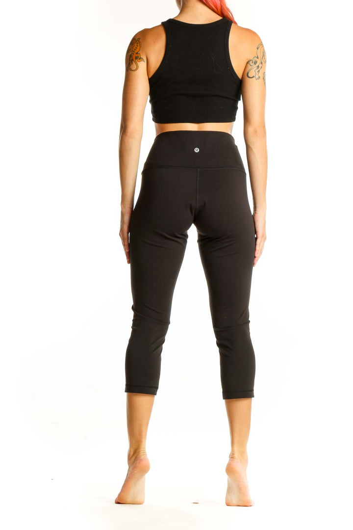 Side view of woman wearing black Lululemon high-waisted capri leggings and crop top
