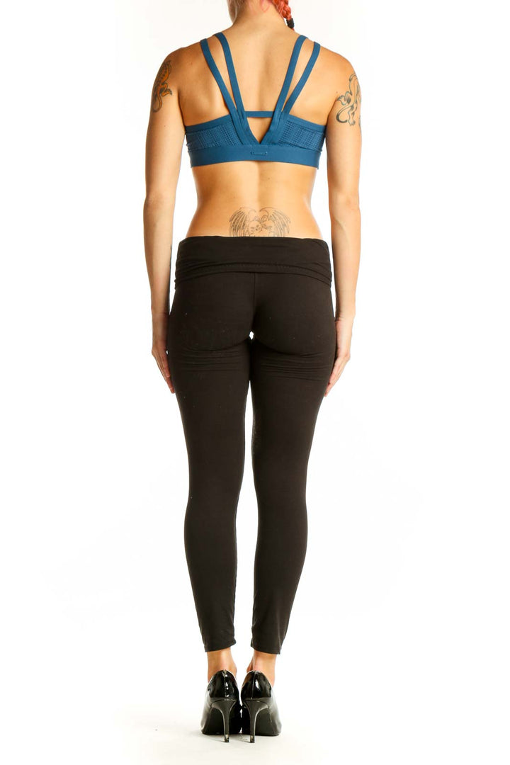 Side view of woman wearing blue Under Armour sports bra with black leggings