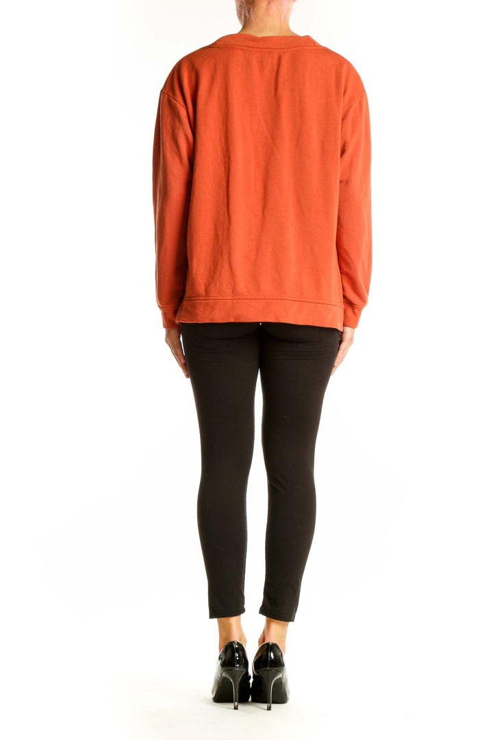 Side view of orange Orvis V-neck long sleeve top on model with black pants