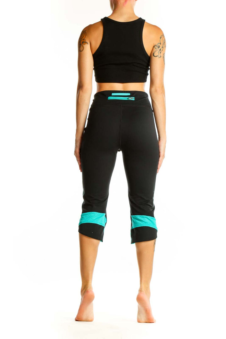Side view of woman wearing black Under Armour capri leggings with teal cuffs