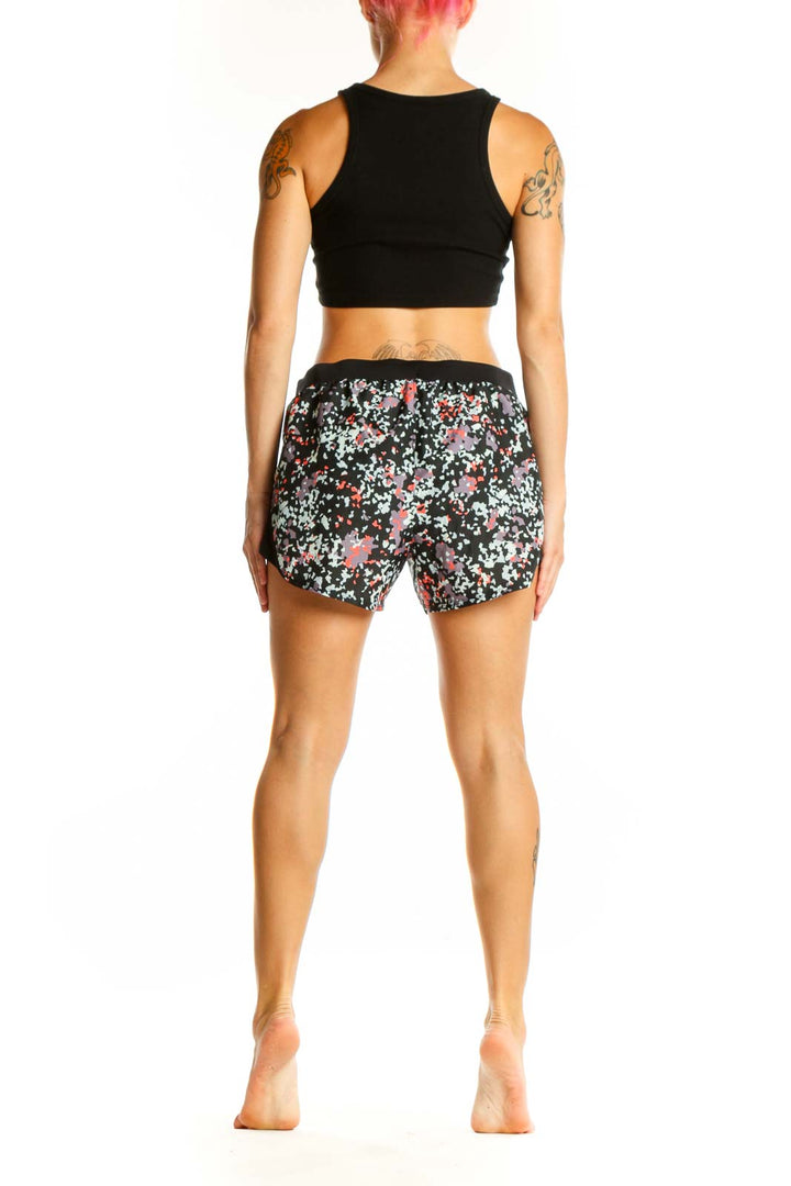 Side view of woman wearing black floral print Under Armour athletic shorts with black crop top