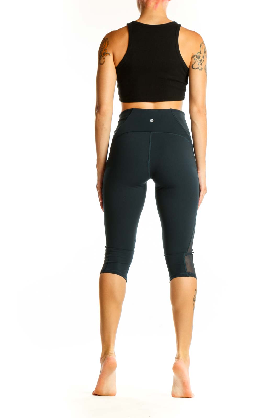 Side view of woman wearing Lululemon dark green capri leggings and black crop top