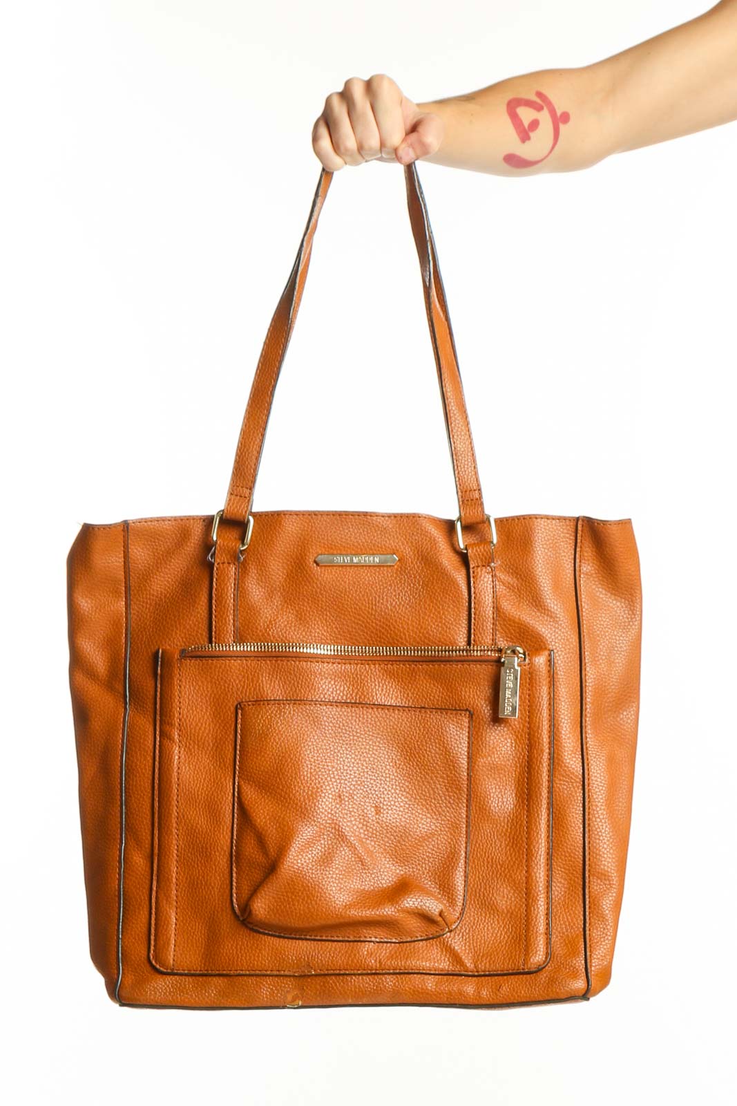 Orange leather tote bag by Steve Madden with front pocket and dual shoulder straps, held by a woman's hand