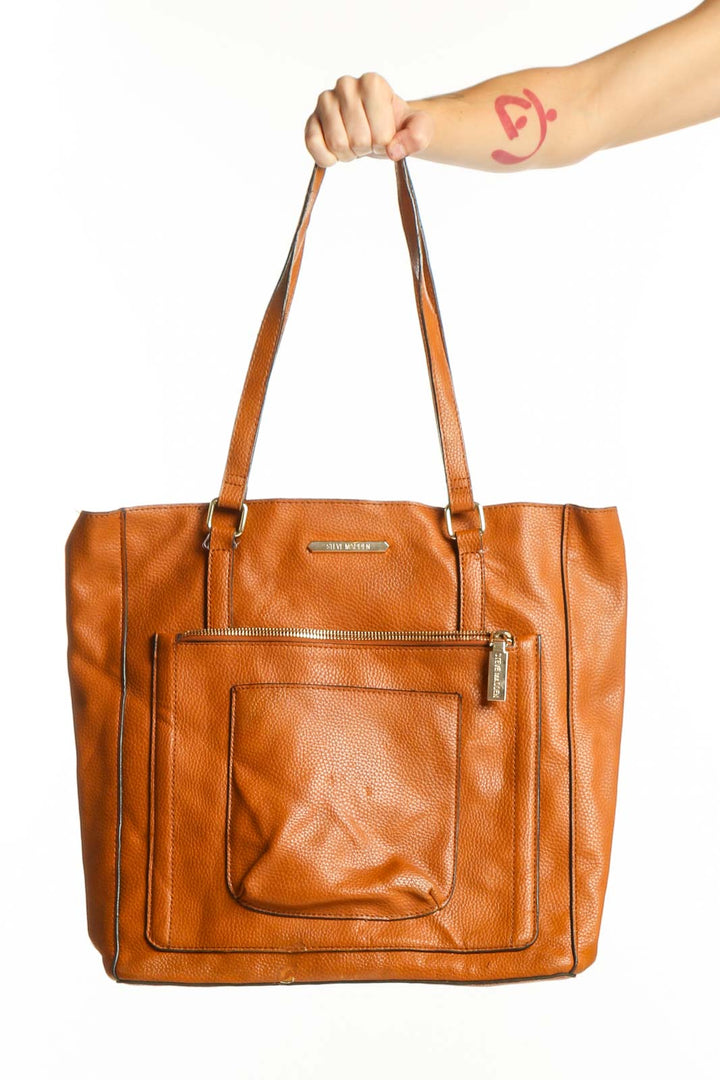Orange leather tote bag by Steve Madden with front pocket and dual shoulder straps, held by a woman's hand