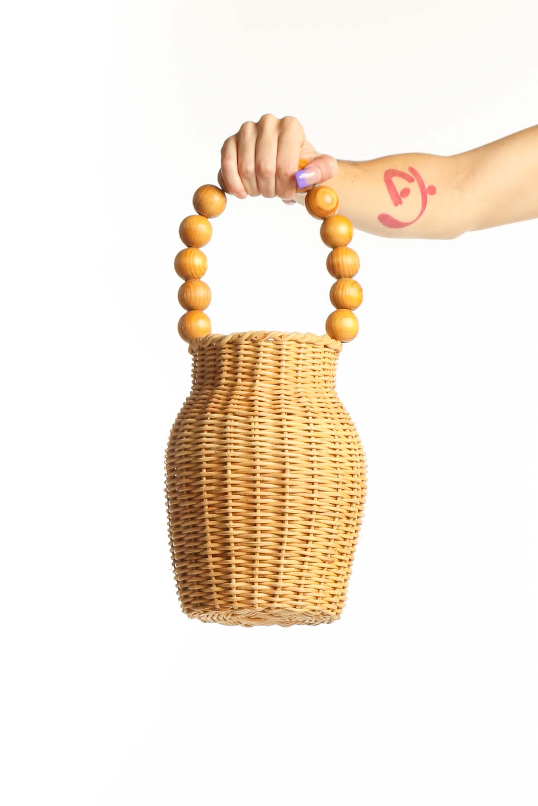 Natural wicker woven clutch with golden wooden bead handles held in hand, showing front view and textured weave detail