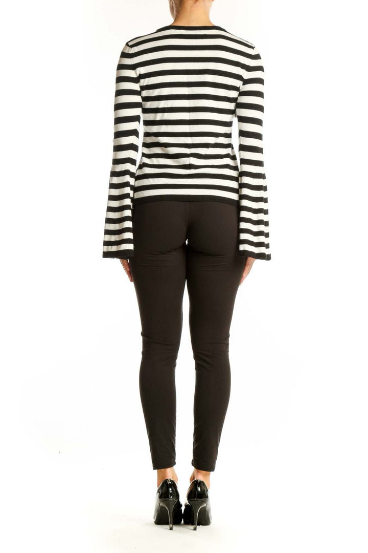 Side view of model wearing Milly Black and White Striped Bell Sleeve Knit Top with black pants